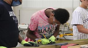  Young men working in a woodshop with safety goggles and bright colored clothing